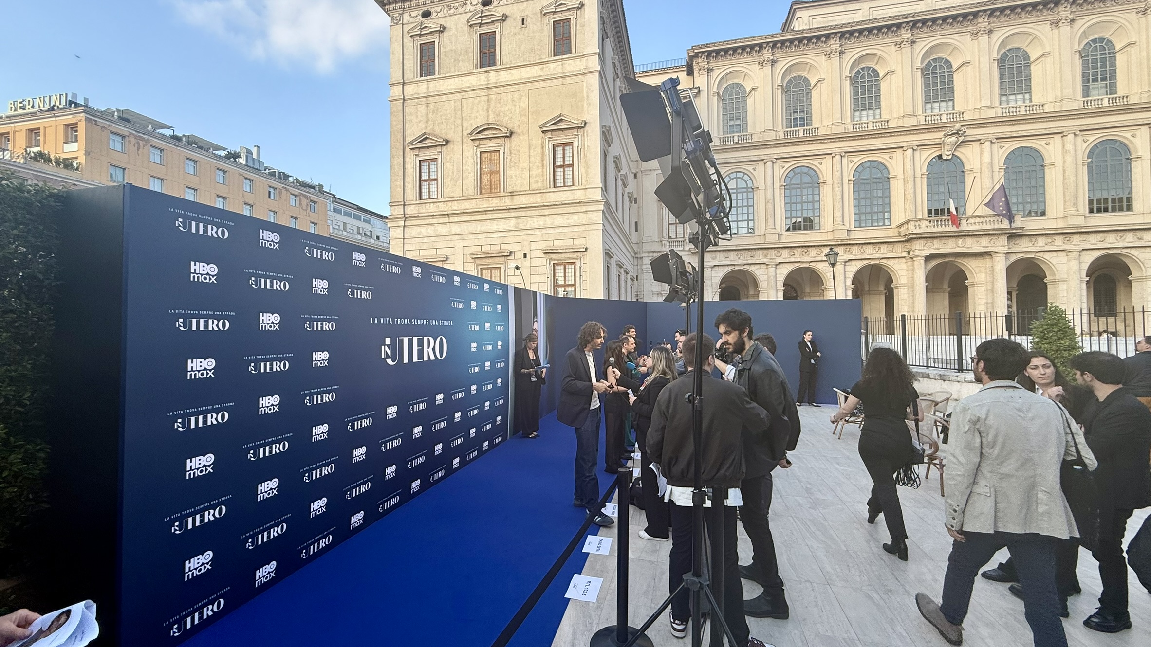 Area photocall della première di In Utero, con fondale personalizzato, tappeto blu e fari su stativo.