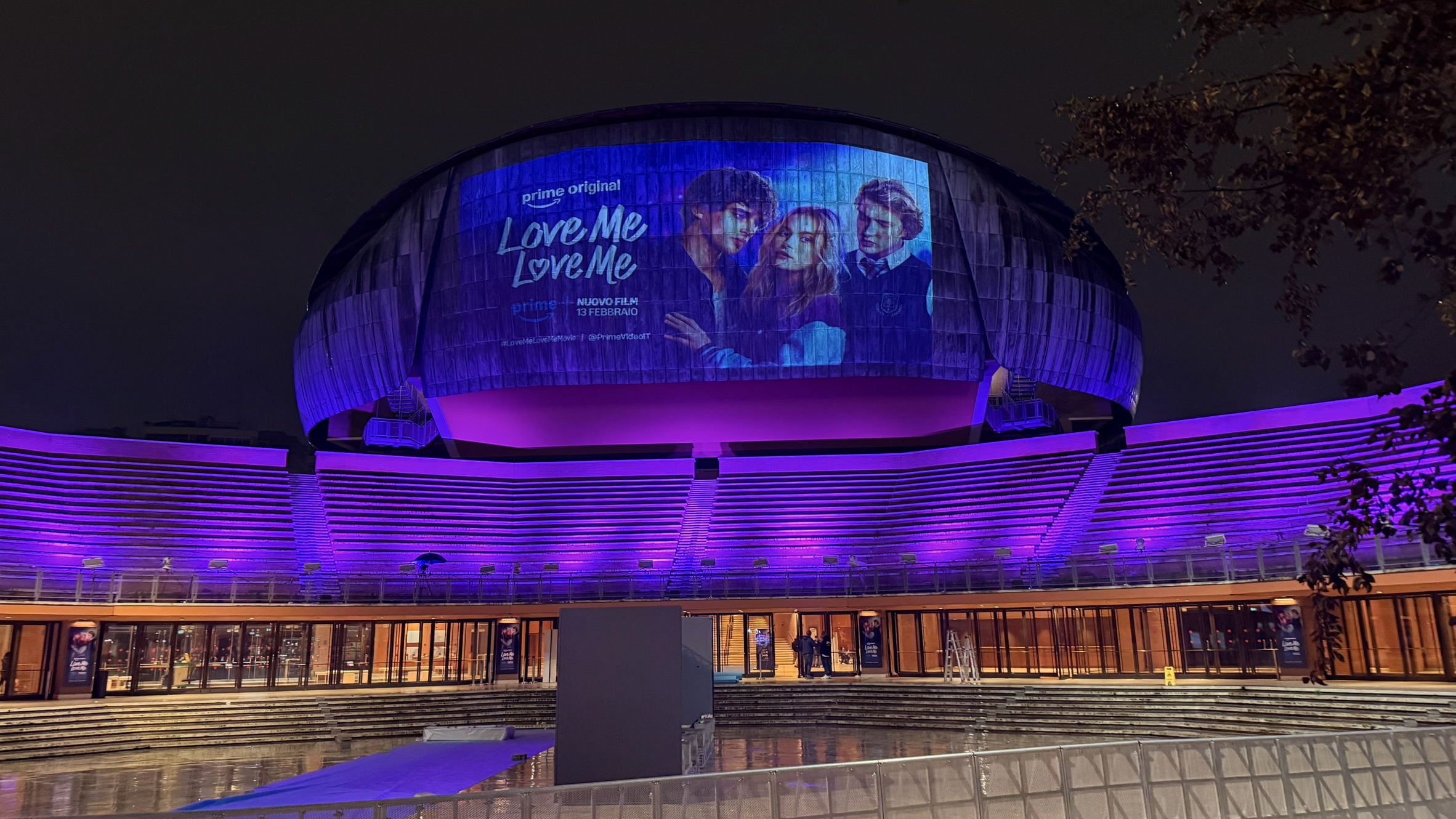 Proiezione di Love Me Love Me sulla facciata di un edificio e illuminazione architetturale viola delle gradinate.
